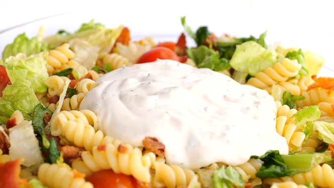 adding dressing to pasta salad